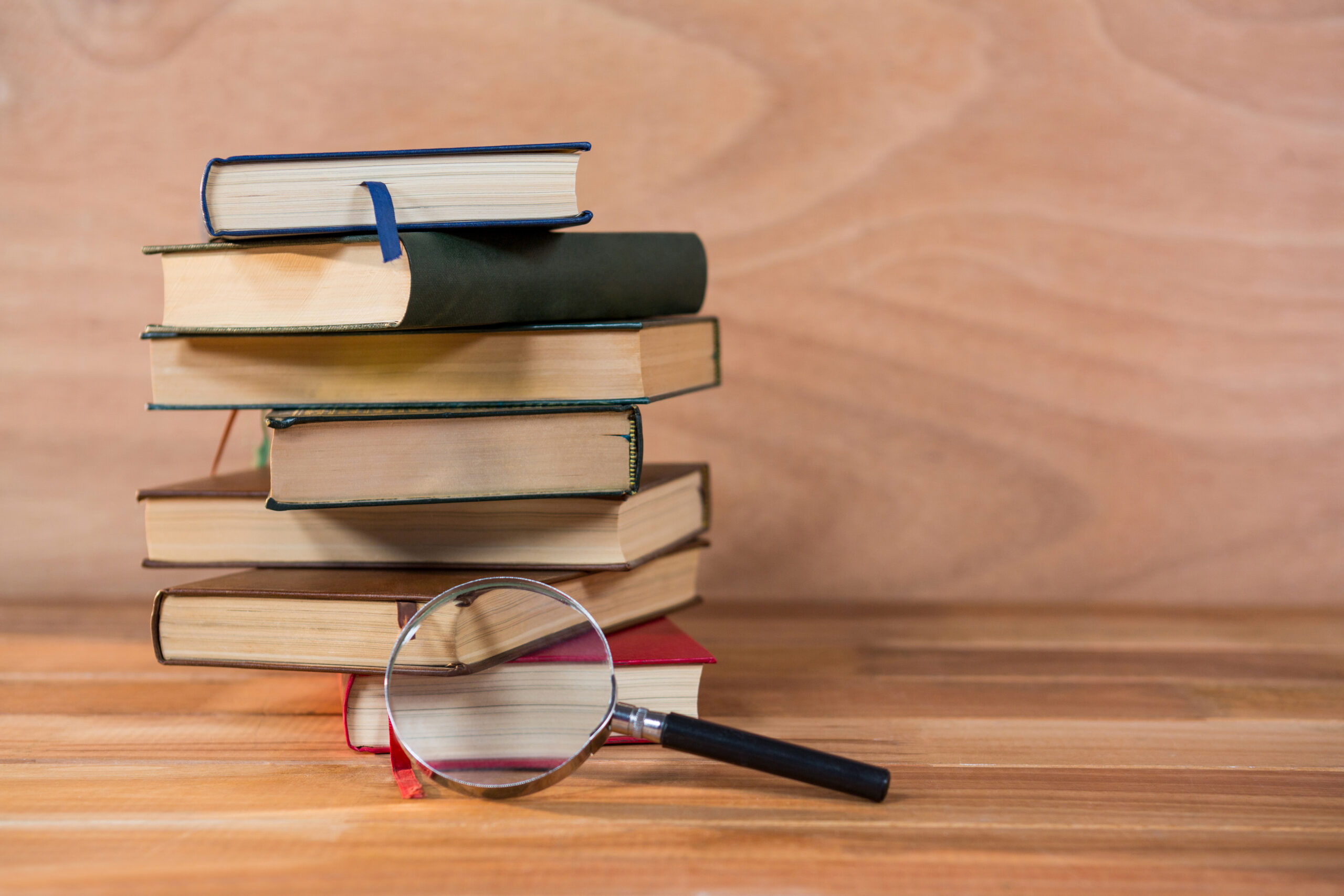 Magnifying glass with stack of books on a wooden table